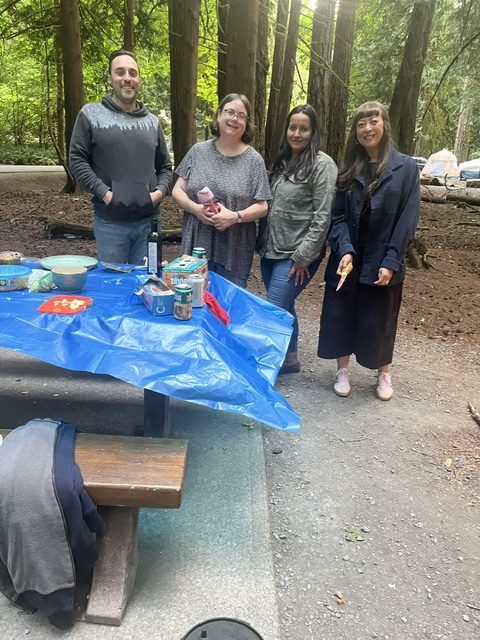 Four members posing together by the picnic table at the campsite